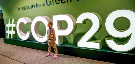 طفل يقف أمام الشعار المضيء #COP29 