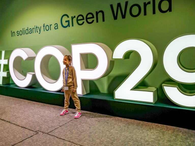 Un niño frente al cartel luminoso de #COP29. 