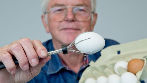 Ein Mann hält ein Ei mit einem Eierhalter in der Hand Ein Mann hält ein Ei mit einem Eierhalter in der Hand